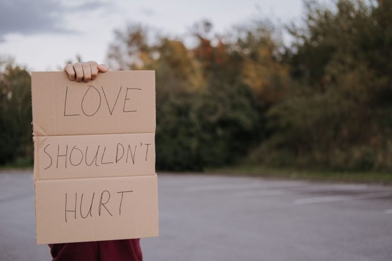 Crop anonymous person demonstrating carton signboard with slogan love should not hurt on blurred background of asphalt road and trees